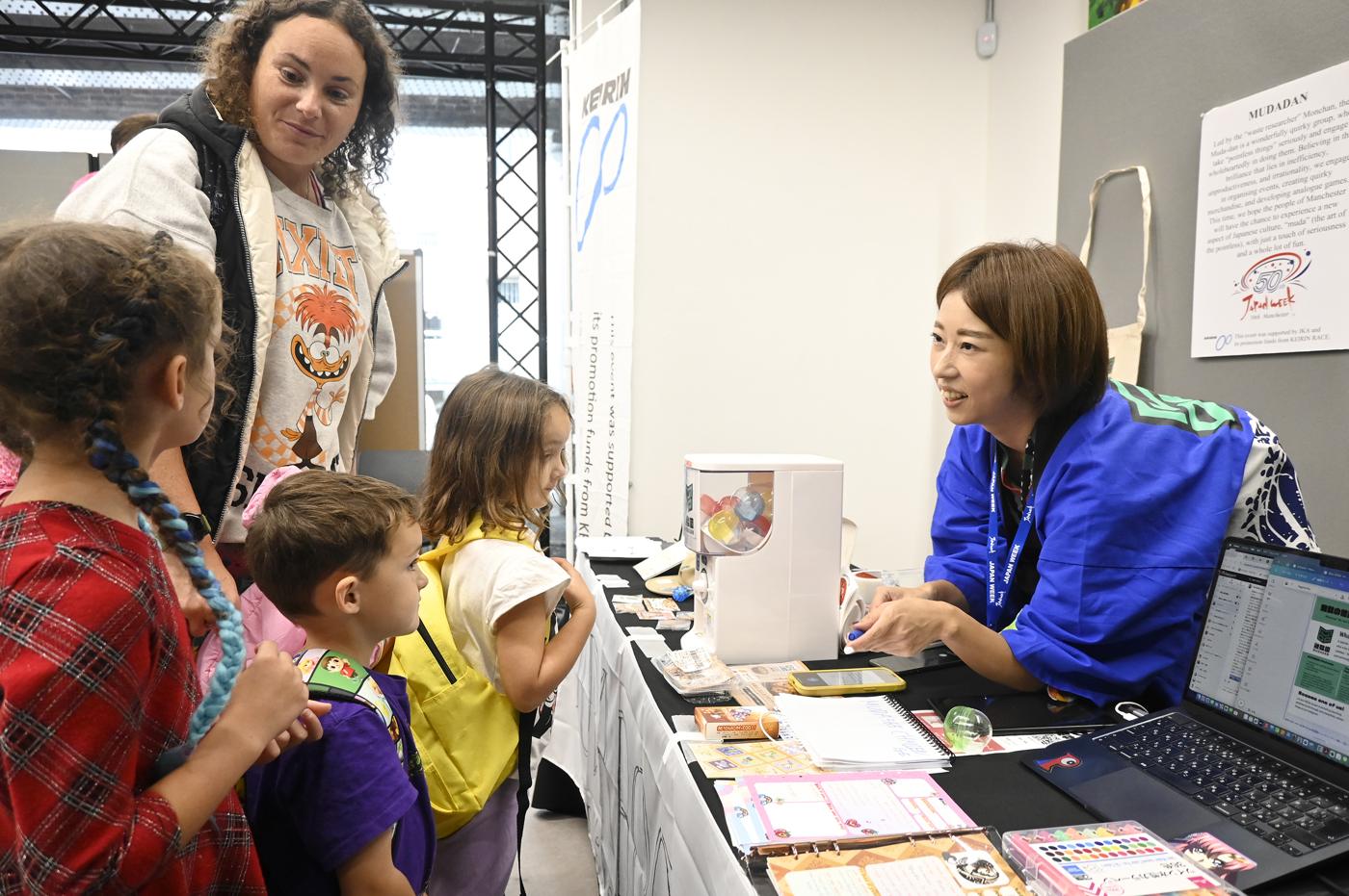 Children and parents gathered around the MUDADAN booth, reading the MUDADAN poster.