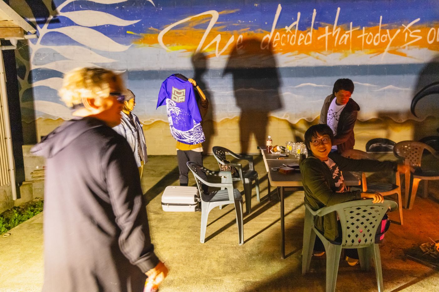 Members holding up a MUDADAN happi coat in front of a mural at night