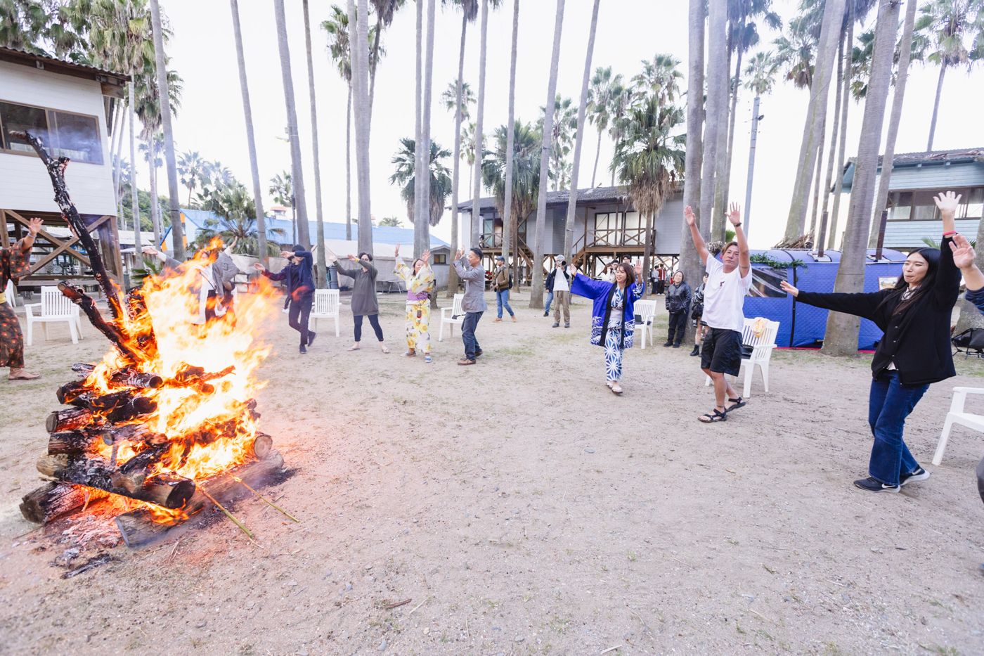 People dancing around a large bonfire under palm trees